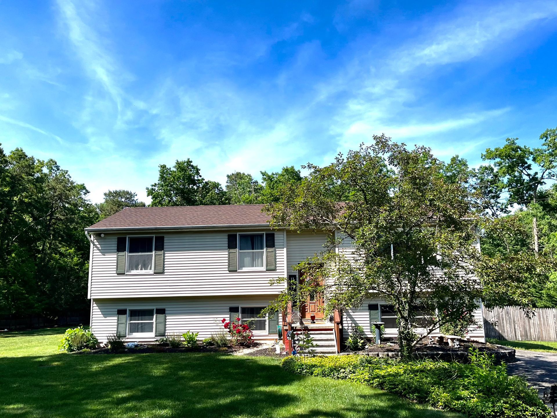 A large white house with a brown roof is surrounded by trees on a sunny day.
