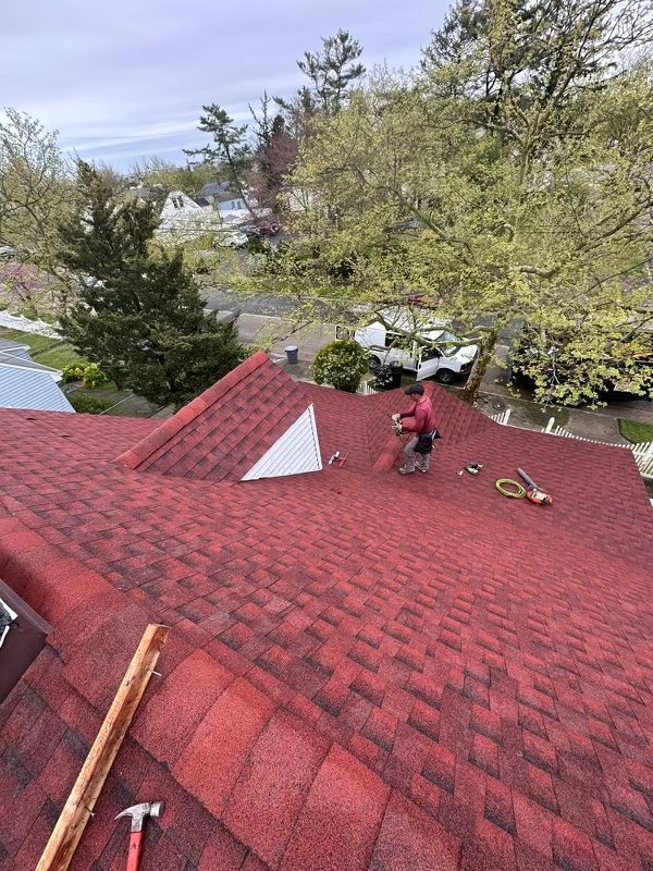 A man is standing on top of a red roof.