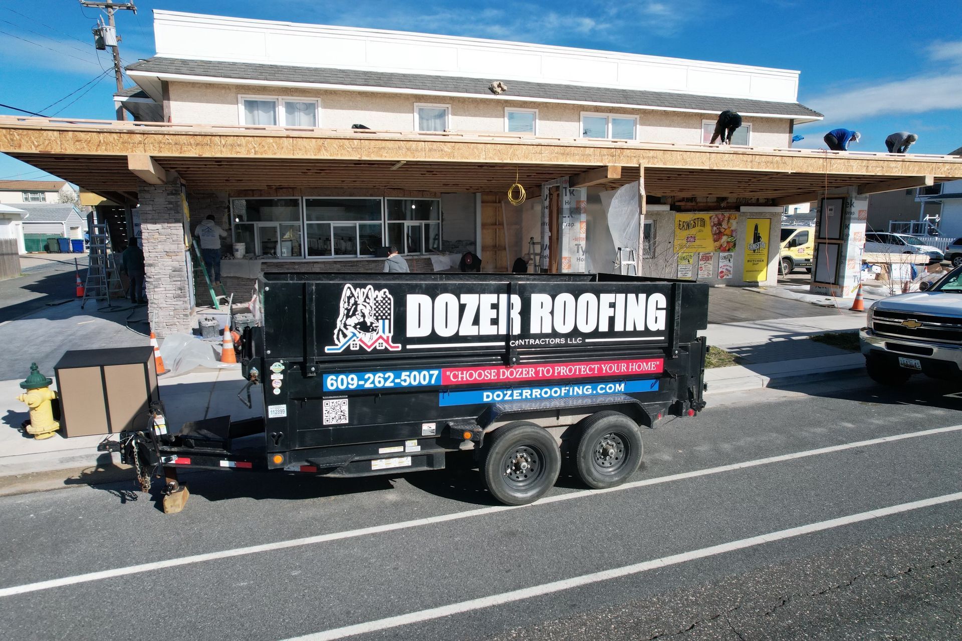 A dozer roofing dumpster is parked in front of a building