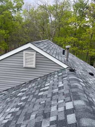The roof of a house with a gray siding and a gray shingle roof.