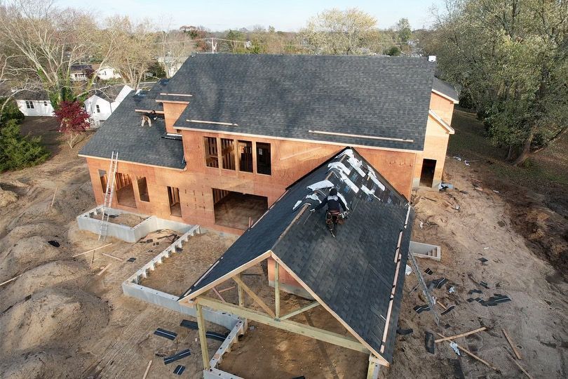 An aerial view of a house under construction with a roof being installed.