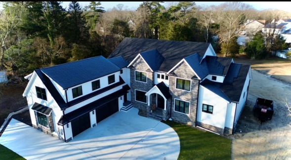 An aerial view of a large white and black house with a black roof.