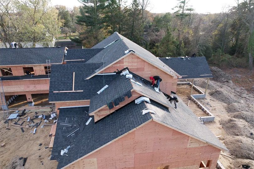 An aerial view of a house under construction with a man working on the roof.