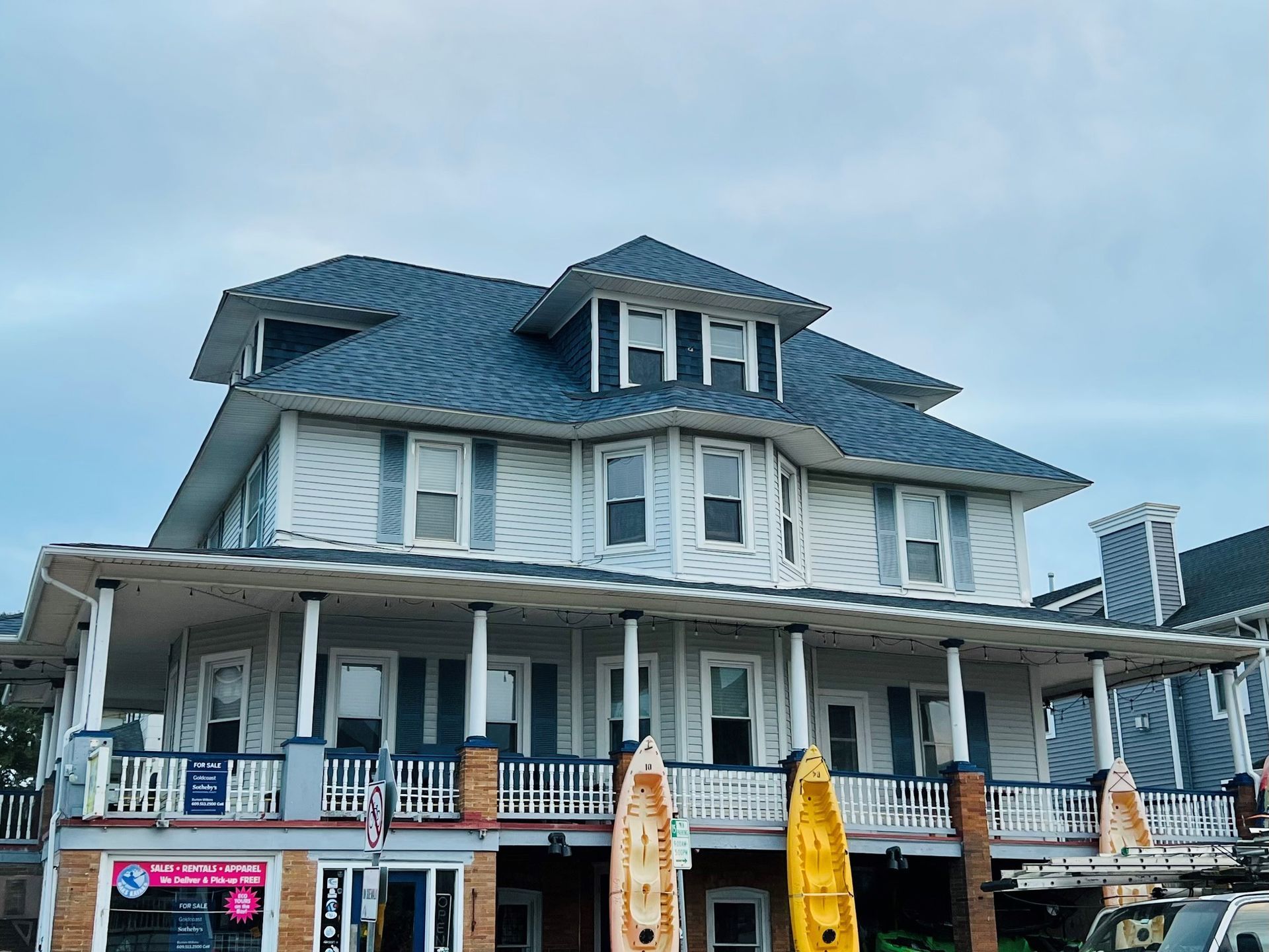A large white house with a blue roof and kayaks on the porch.