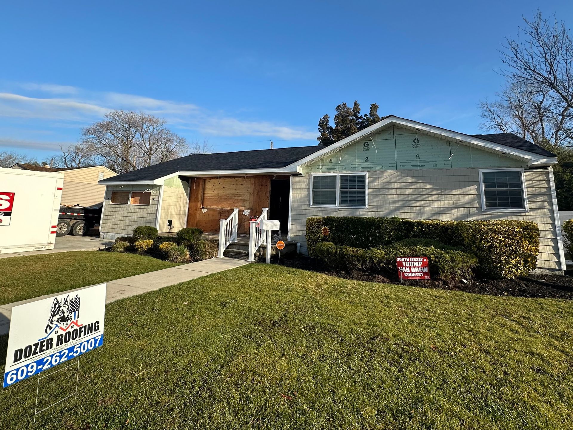 A white house with a black roof and a sign in front of it.