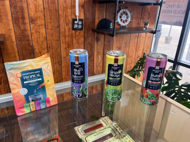 Colorful product display on a glass table with three tall drink cans and a package in a wood-paneled room
