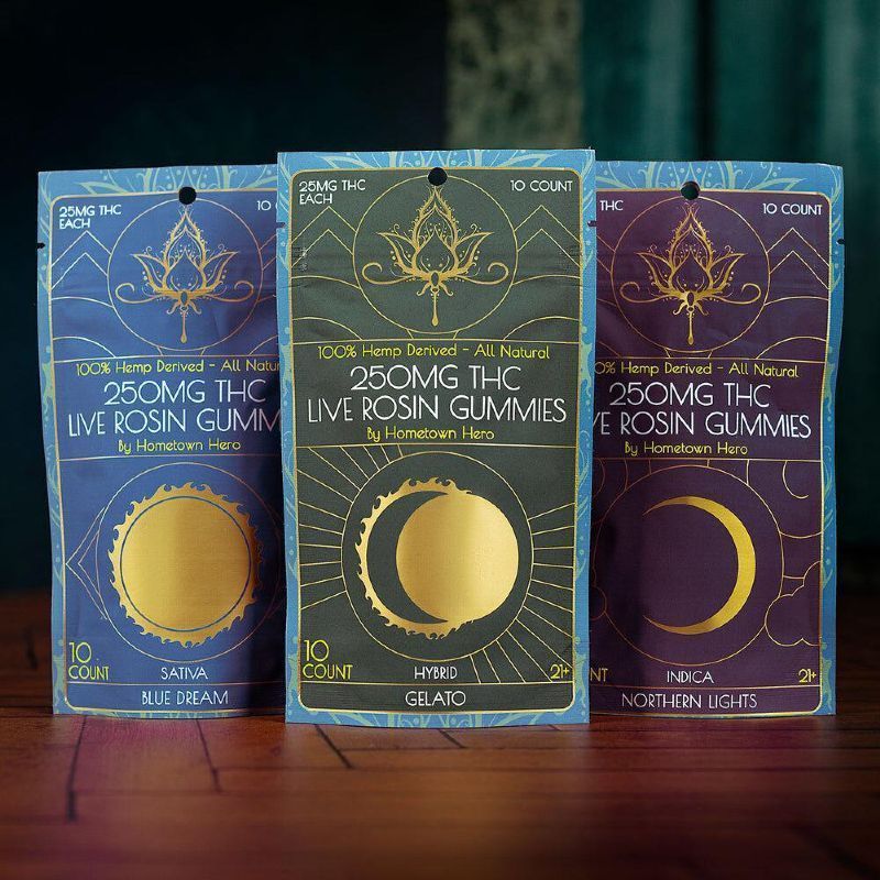 Three THC live rosin gummy boxes in blue, green, and purple on a wooden table.