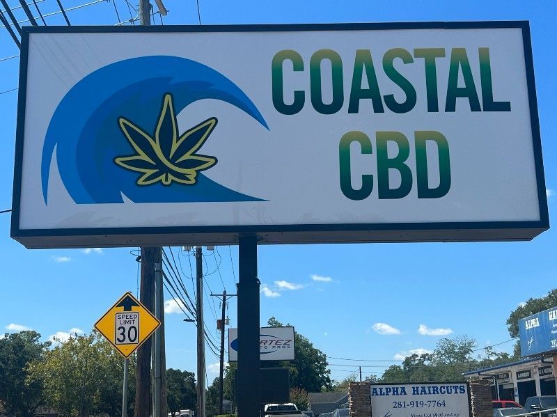 Coastal CBD roadside sign with a blue wave and cannabis leaf logo under a sunny sky