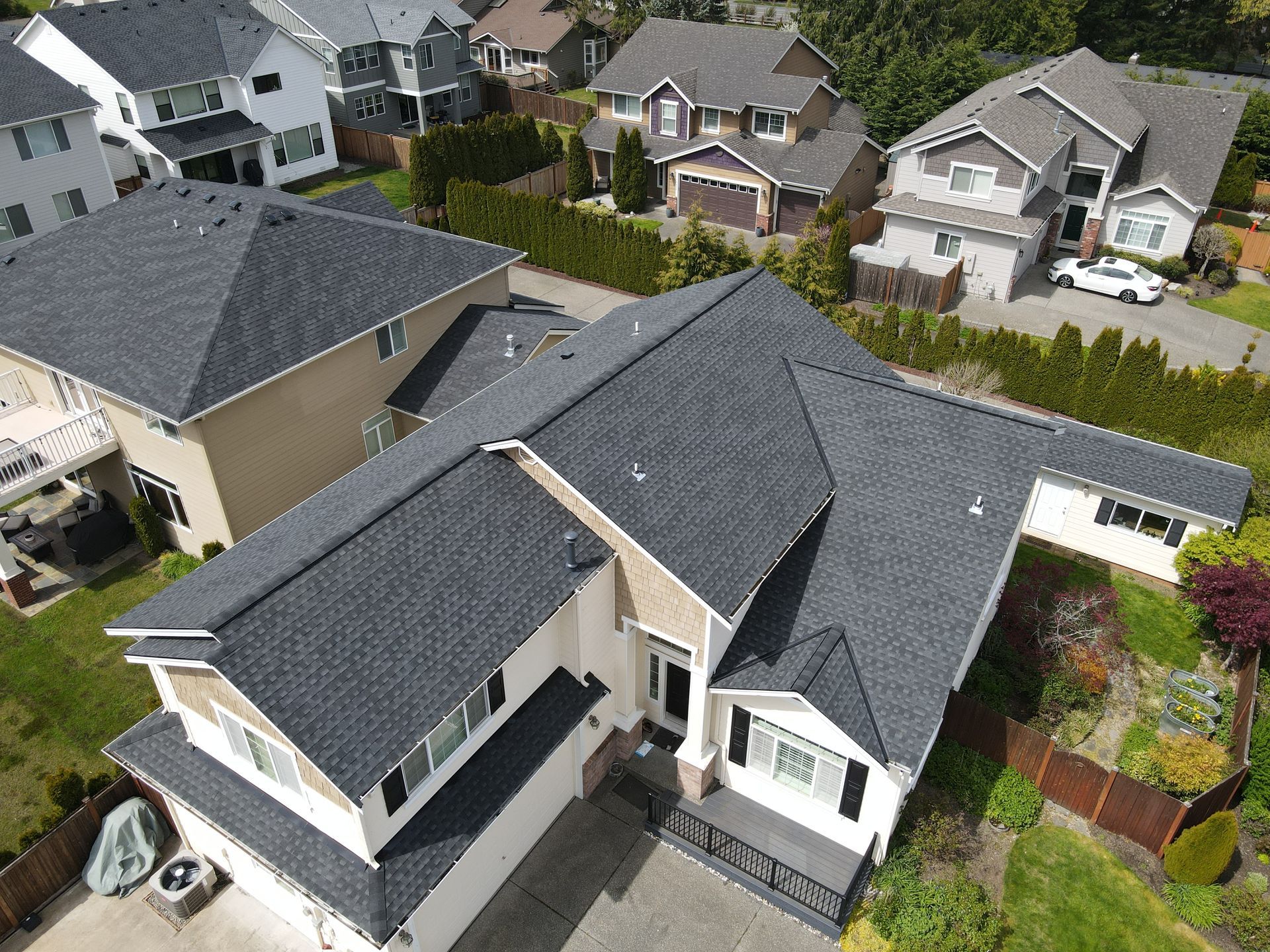An aerial view of a house with a black roof in a residential area.