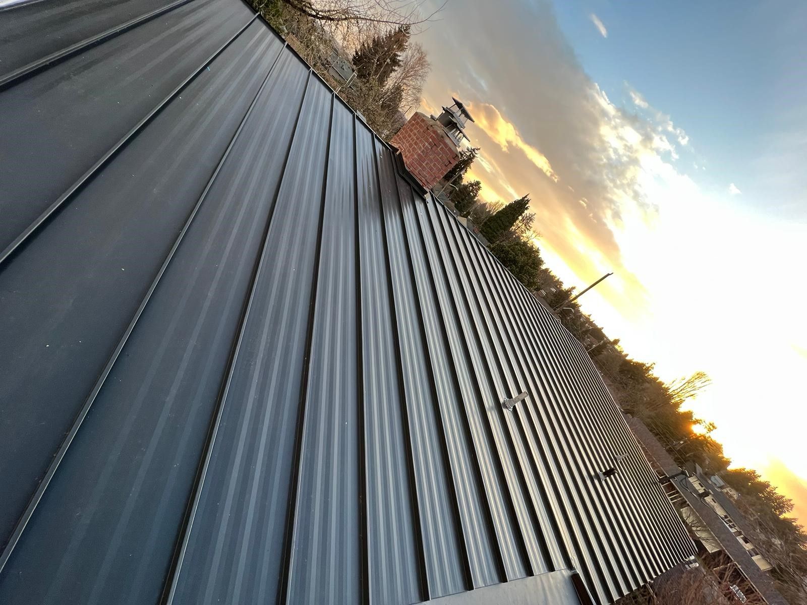 A roof with a chimney on top of it and a sunset in the background.