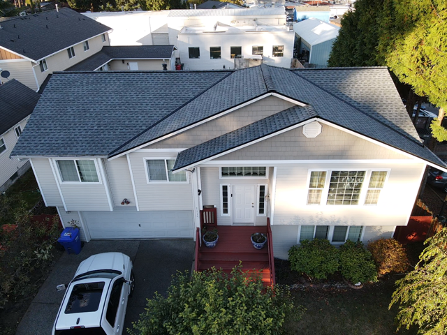Aerial view of a gray-roofed house with white siding, a red front porch, and a car in the driveway.