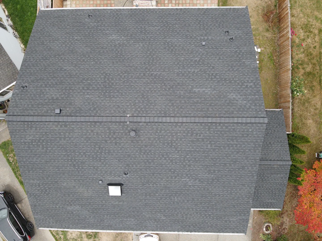 Overhead view of a dark gray asphalt shingle roof on a house, with several vents and a chimney.