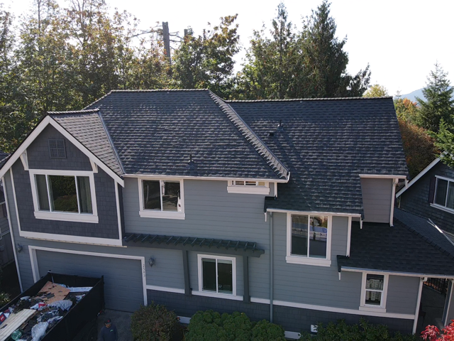 Gray house with dark roof and white trim, surrounded by trees.