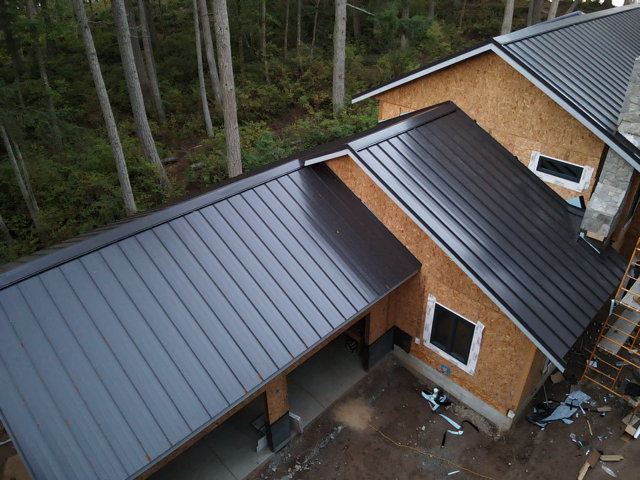 Dark metal roof on a house under construction with a forested background.