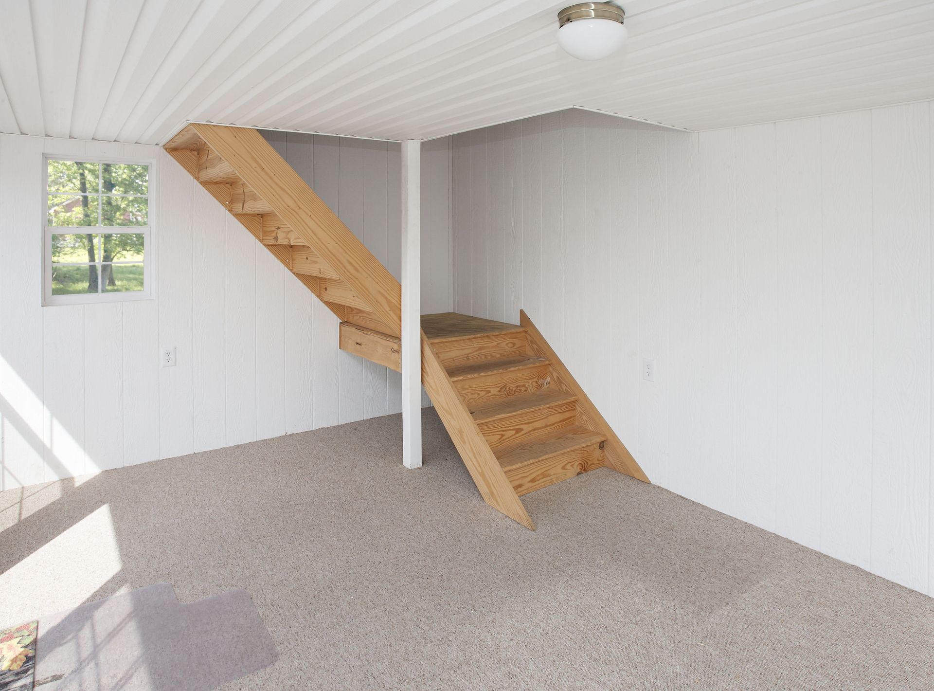 Interior of a building with wooden stairs, white walls, and a window. The floor is covered in speckled gray flooring.