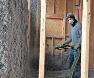 Worker spraying insulation into wall cavity in a framed construction site
