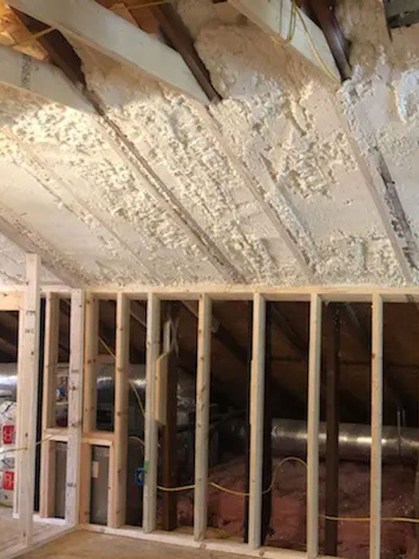 Unfinished attic with spray-foam insulated roof and exposed wooden framing over stud walls
