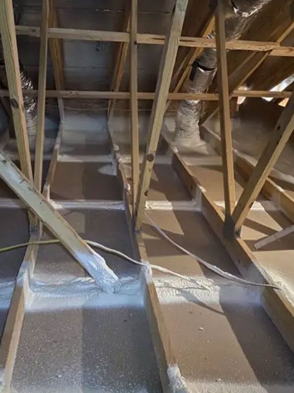 Attic with exposed wooden rafters and ducting, showing insulation-covered floor between joists