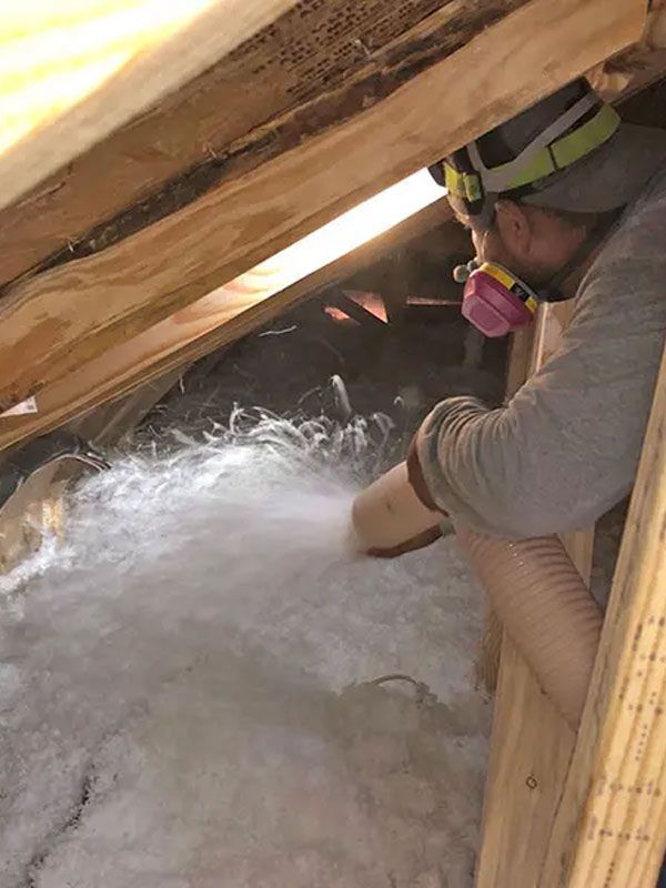 Worker spraying foam insulation into a roof attic space