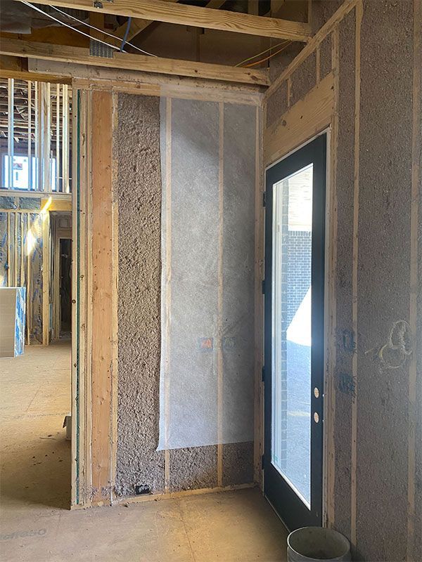 Unfinished interior wall framing with a glass door and a bucket on the floor.