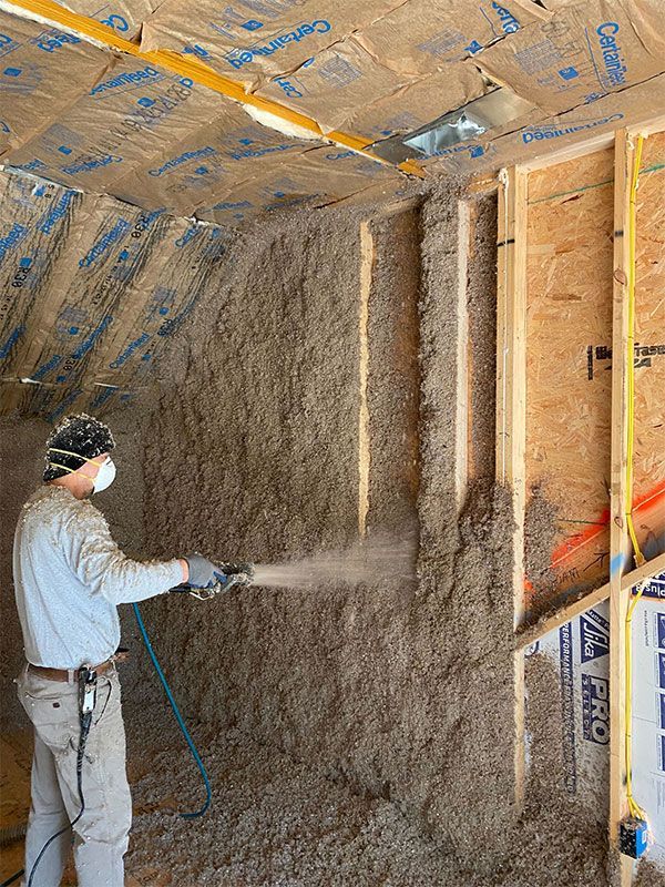Worker spraying insulation onto unfinished interior walls with a hose in a framed room