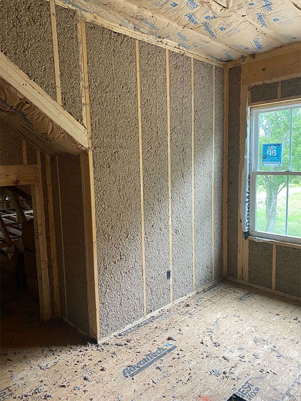 Unfinished room interior with exposed insulation, slanted ceiling, and a window showing a green yard.