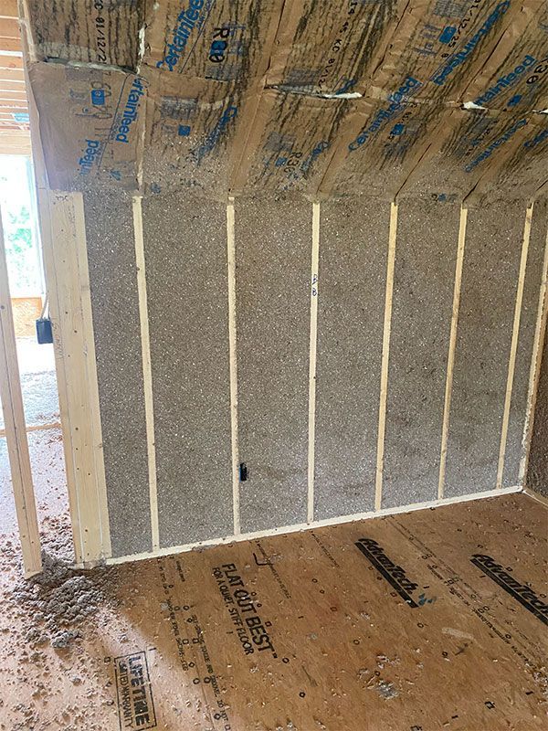 Unfinished interior wall insulation with vertical white studs and a bare plywood floor.