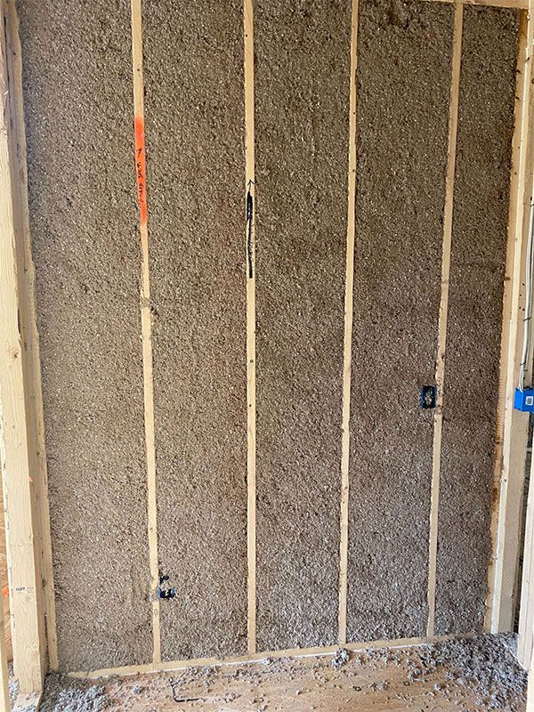 Unfinished wall with exposed insulation and vertical wooden studs in a construction area