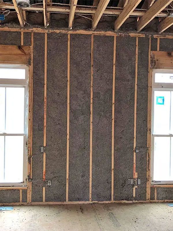 Unfinished room wall with exposed wooden studs, insulation, and two narrow windows.
