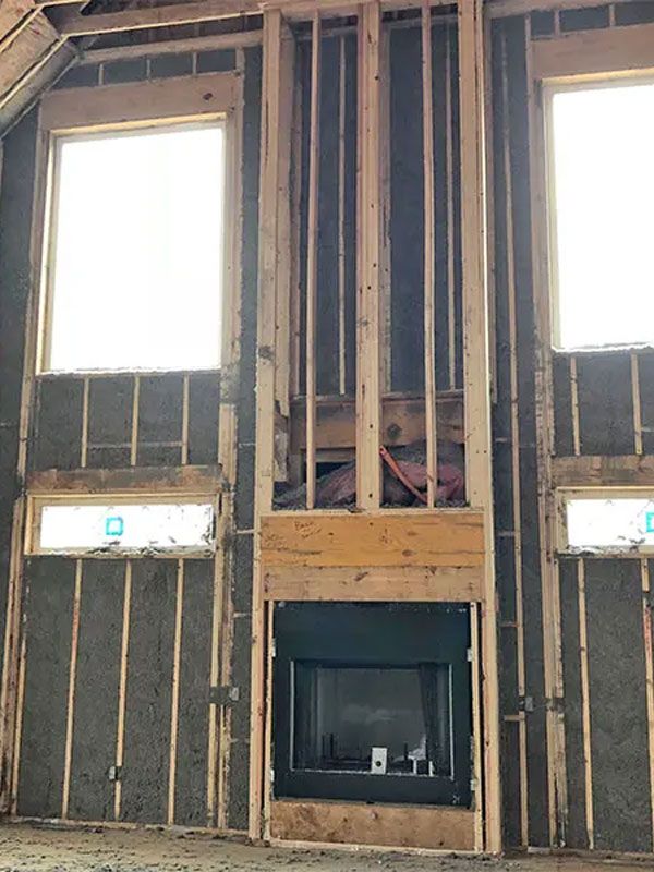 Exposed interior wall framing with two windows and a fireplace opening under construction.