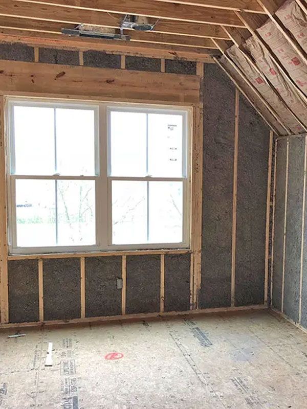 Unfinished attic room with exposed insulation, sloped ceiling, and a window letting in daylight