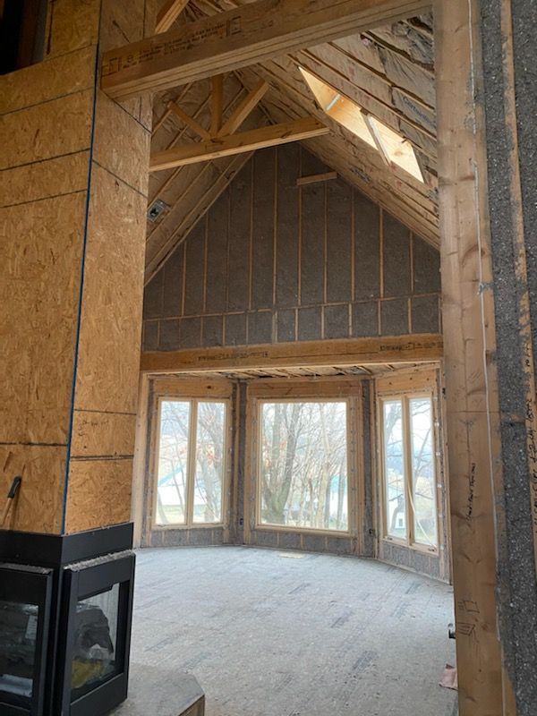 Unfinished vaulted room with exposed wood framing, large windows, and a black fireplace in the corner