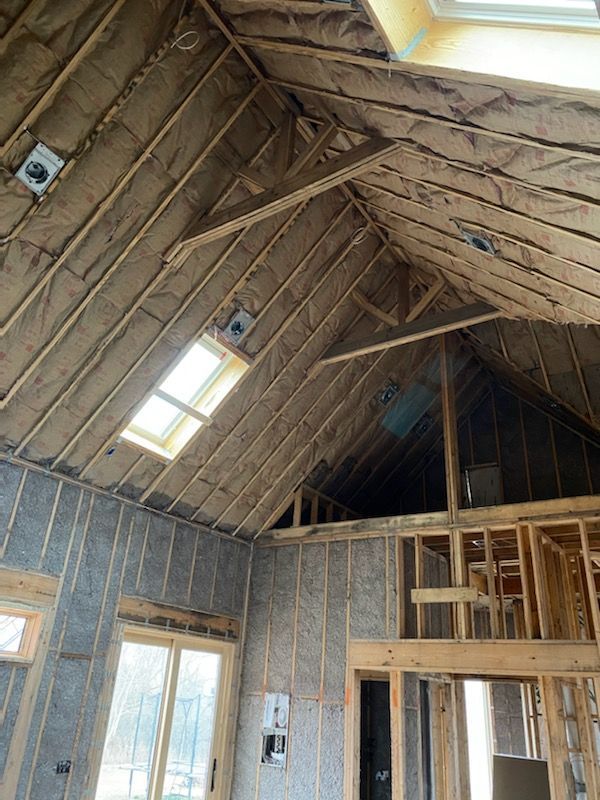 Insulated attic with exposed wood framing, skylight, and windowed wall under construction
