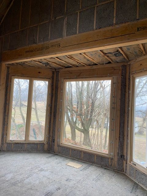 Empty unfinished room with large bare windows, exposed wood framing, and a dusty concrete floor.