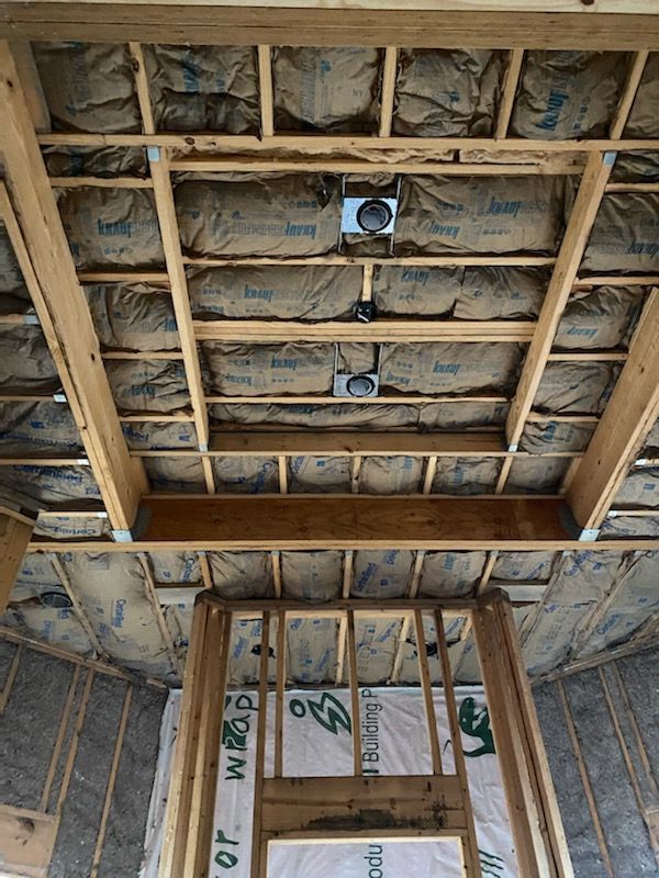 Exposed ceiling framing with insulation batts and two recessed electrical boxes under construction