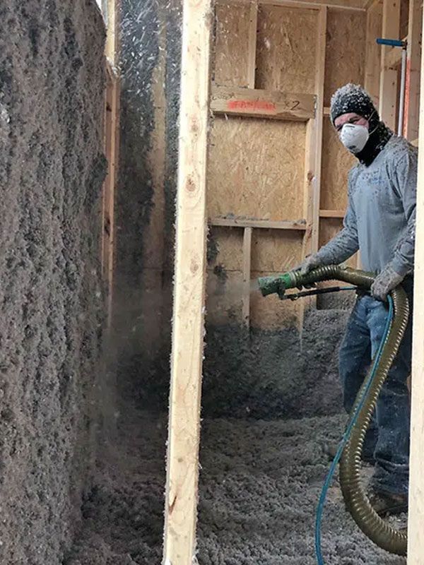 Worker spraying insulation foam inside a wall cavity, wearing a mask and gloves