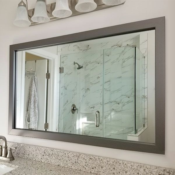 Bathroom mirror above sink reflecting a glass shower with marble-pattern tile and gray frame