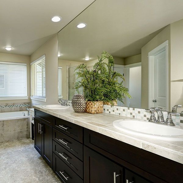 Modern bathroom vanity with double sinks, dark cabinets, large mirror, and potted plant decor