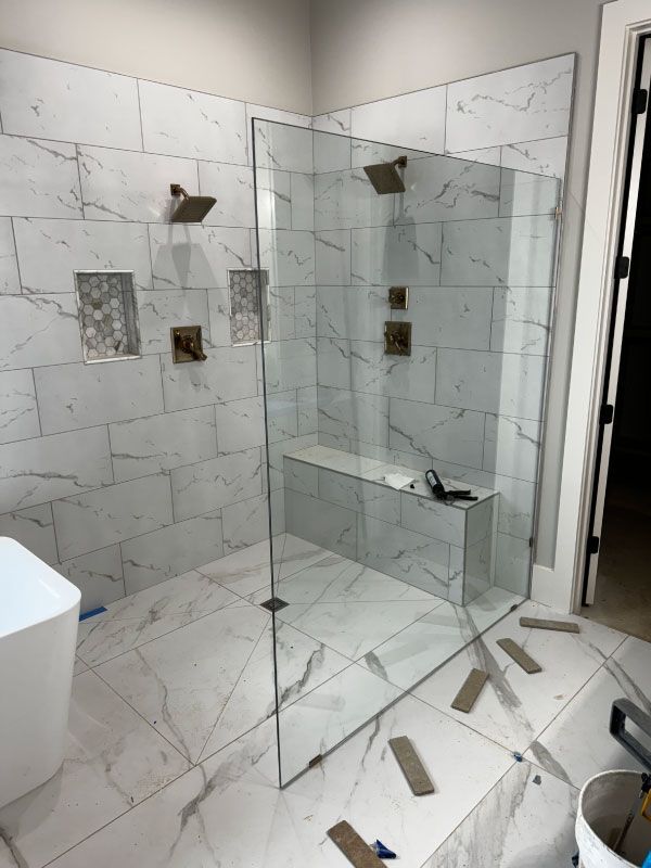 Modern tiled shower with glass enclosure, built-in bench, and loose floor tiles in a bathroom under renovation