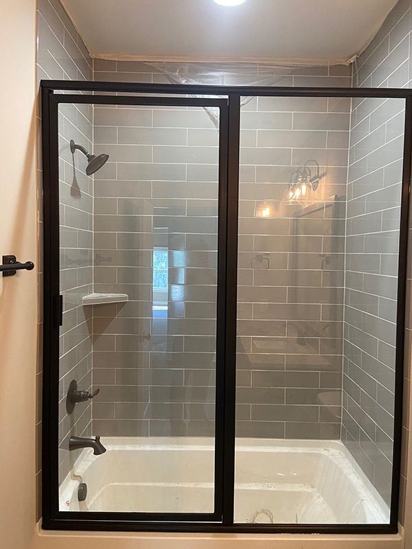 Glass-enclosed bathtub with tiled shower walls and black frame in a bathroom