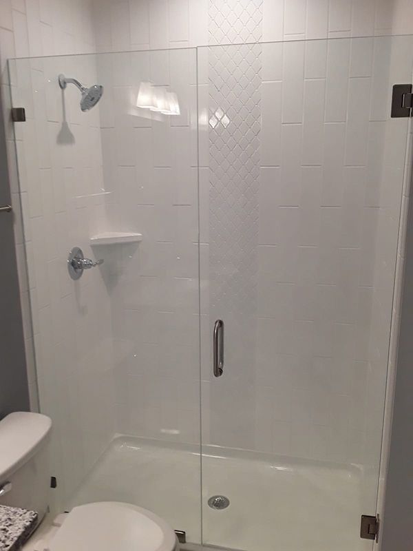 Accessible bathroom shower with glass door, white tile walls, grab bar, and built-in shelf.
