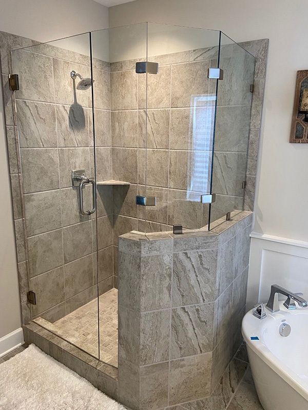 Glass walk-in shower with beige tile and a curved stone bench beside a bathtub.