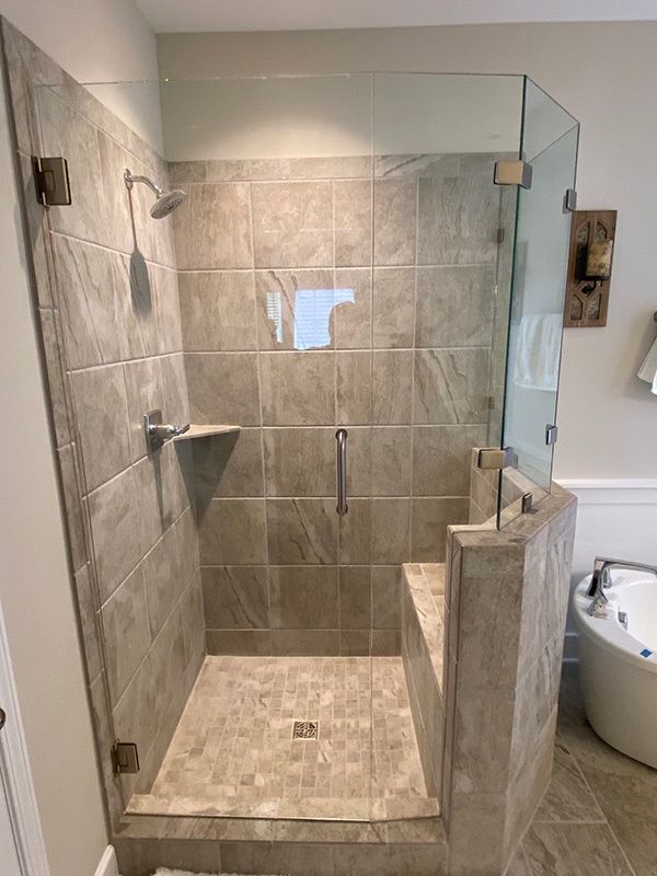 Walk-in tiled shower with glass door, built-in bench, grab bar, and handheld showerhead in a bathroom.