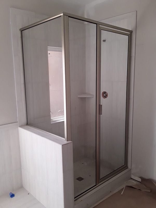 Glass shower enclosure with chrome frame in a white bathroom under construction