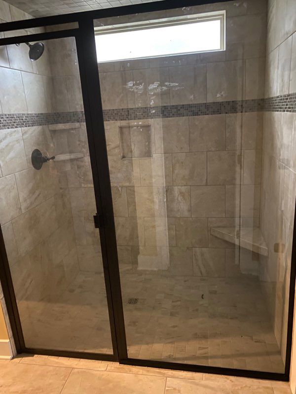 Glass shower enclosure in a tiled bathroom with frosted sliding doors and a small window above.