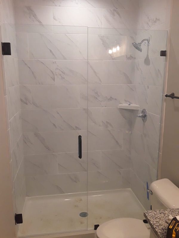 Glass-enclosed walk-in shower with marble tile, built-in shelf, and chrome fixtures
