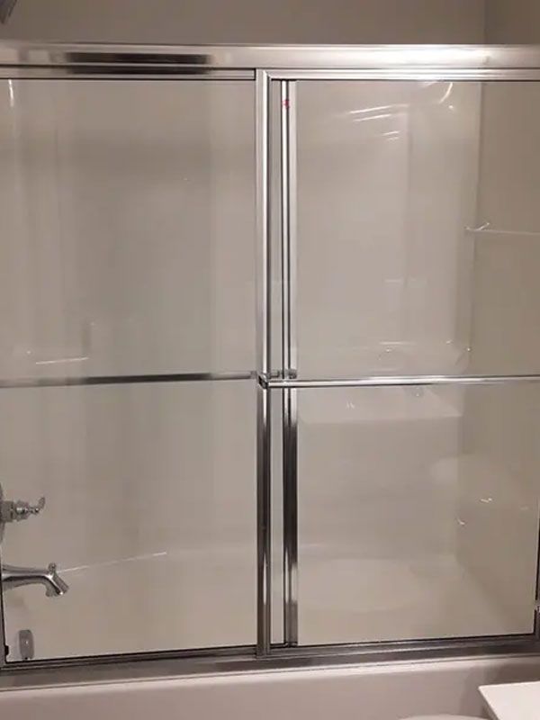 Glass shower enclosure with chrome frame and tiled wall behind it