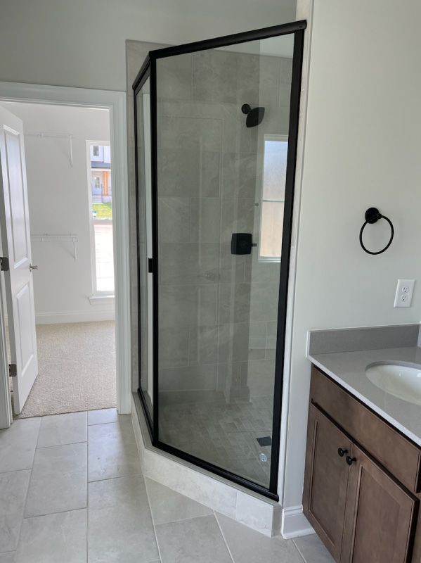 Glass corner shower enclosure in a bathroom with light tile flooring and wood vanity cabinets