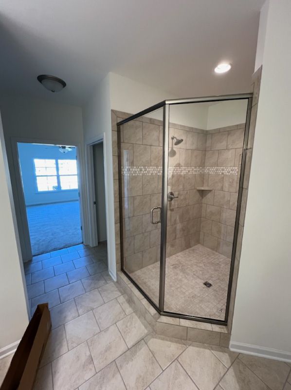 Bathroom hallway with a glass corner shower and tiled floor, lit by recessed ceiling lights
