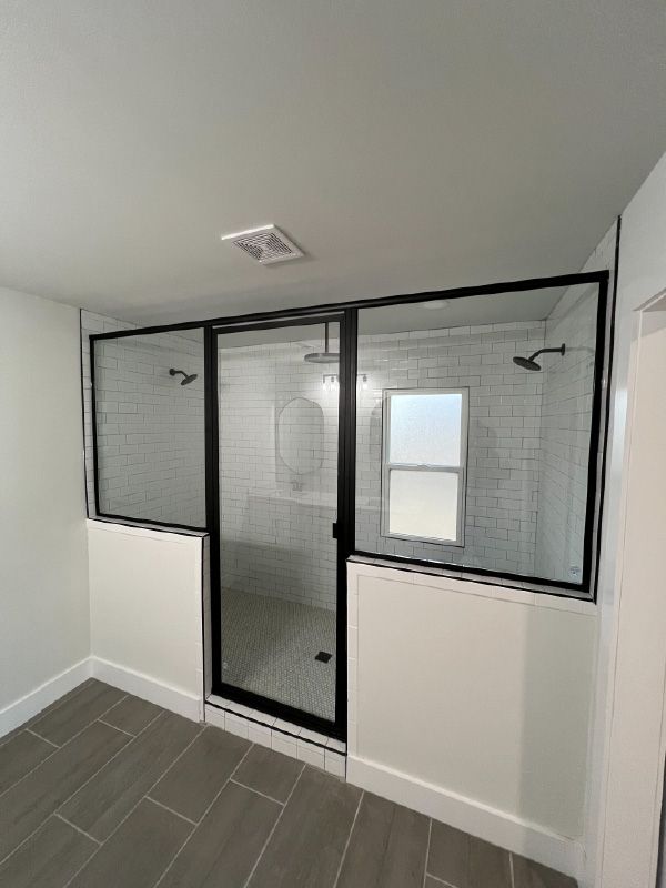 Corner shower enclosure with black-framed glass panels, white walls, and gray tile floor.
